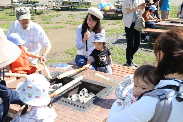 写真:親子が棒に巻いたパンを炭火で焼いている様子